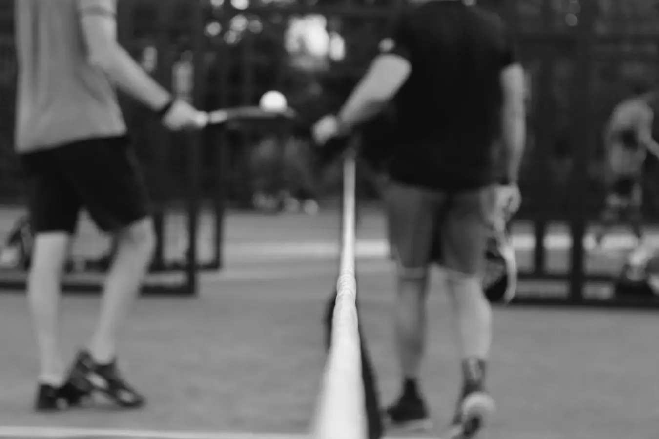 Two padel players walking toward each other at the net after a match, with focus on the net line.