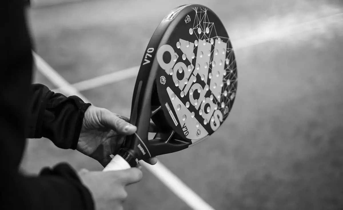 Close-up of a person holding an Adidas V70 padel racket, ready for play, with the court lines visible in the background.