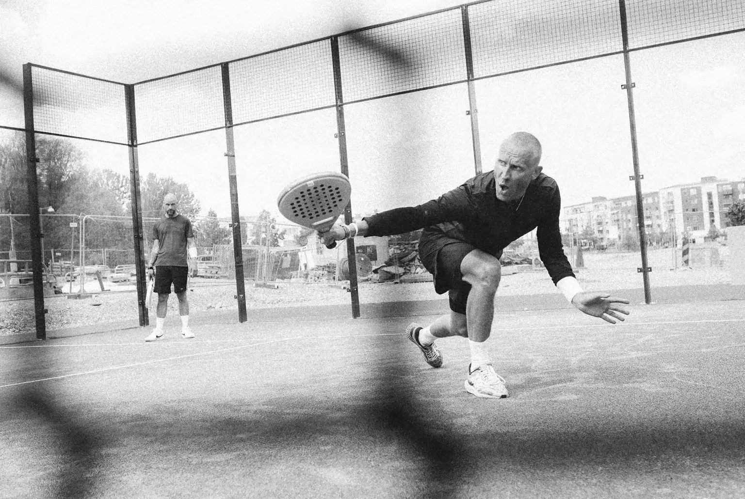 Padel player stretching to counter a lob while his partner stands ready at the back of the court.