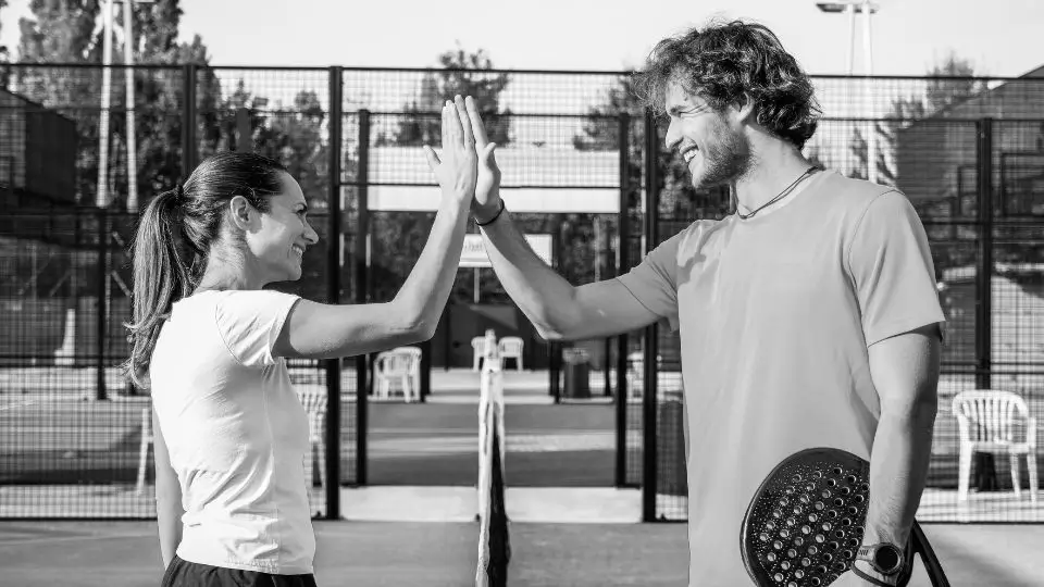 Two padel players high-fiving after a match on the court, celebrating a game well played.