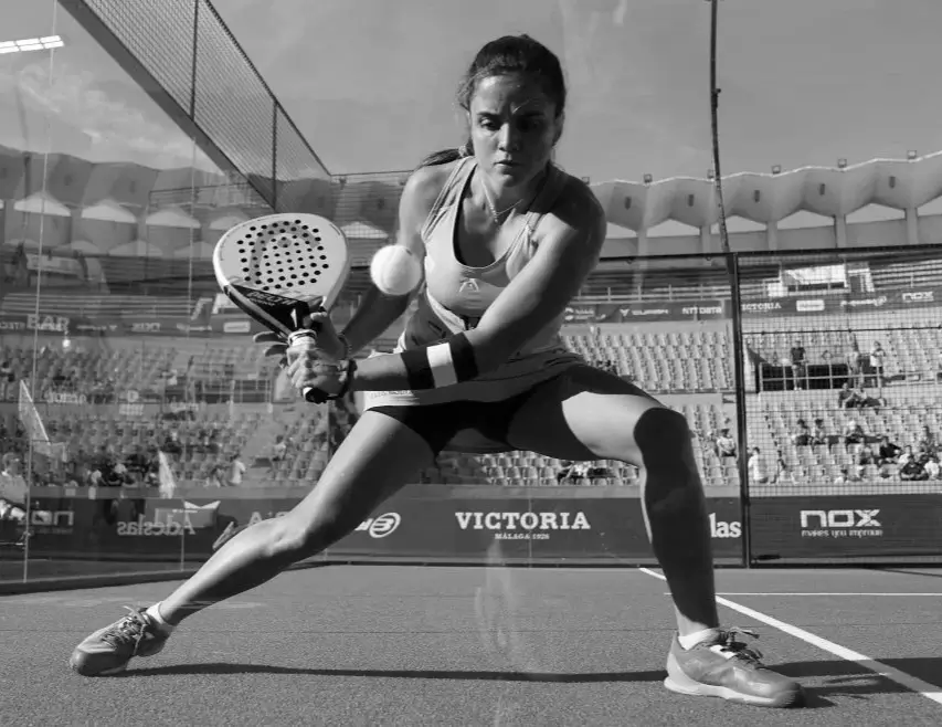 Professional padel player Paula Josemaría executing a powerful two-handed backhand shot during a match on an outdoor court.