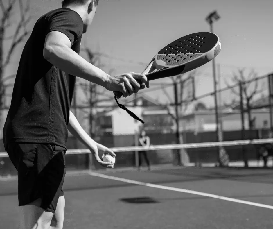 Male padel player preparing to serve with paddle in hand, focused on the court ahead under outdoor lighting.