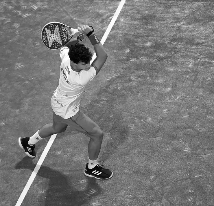 Padel player executing a powerful backhand stroke on the court during a match, showcasing precise technique and focus.