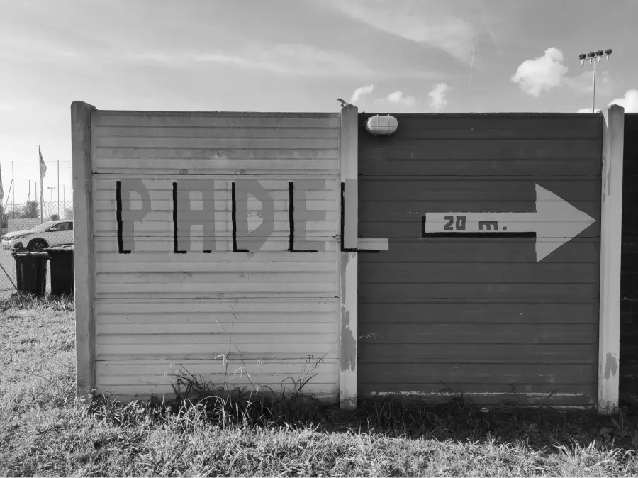 Directional sign on a wall pointing toward a padel court, with a clear arrow indicating 'Padel 20m' under a sunny sky.